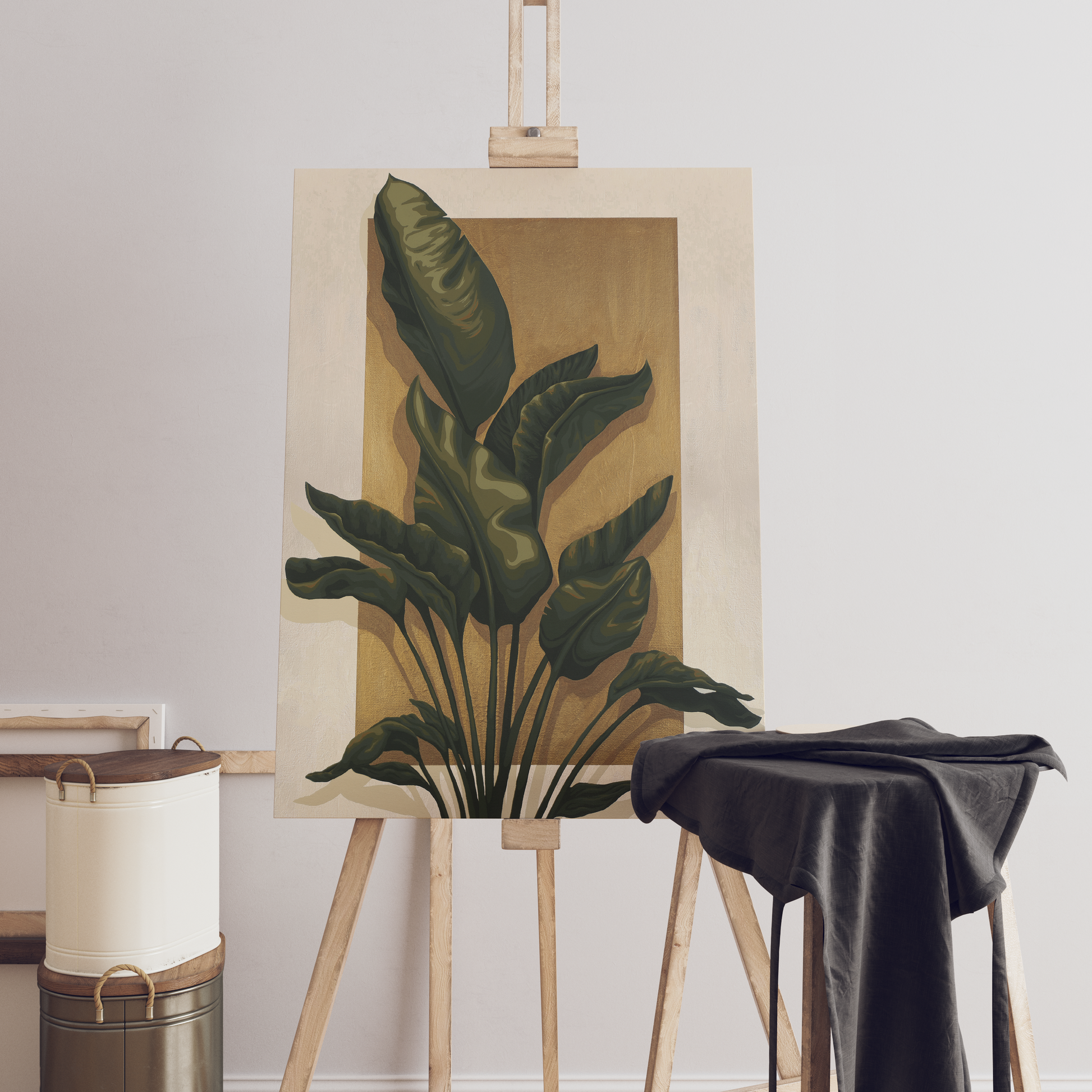 A botanical painting of large green tropical leaves on a warm beige background, displayed on a wooden easel in a minimalist studio setting with a draped black cloth and paint cans.